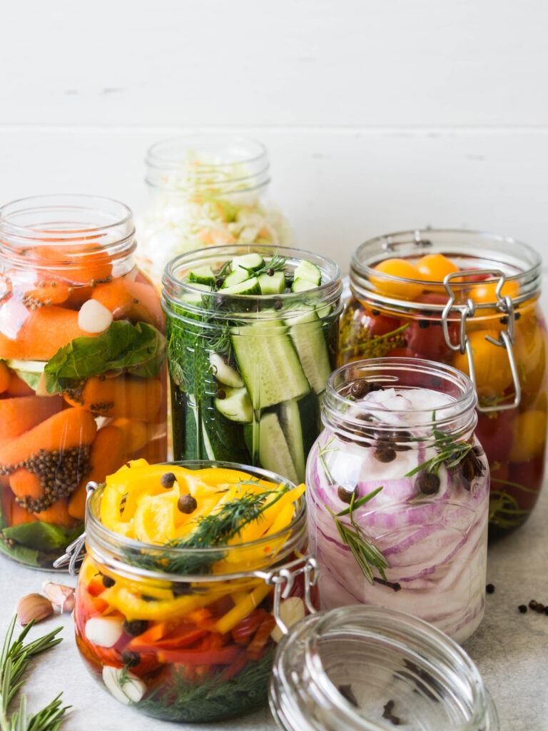 Pickled vegetables. Salting various vegetables in glass jars for long-term storage. Preserves vegetables in glass jars.  Variety fermented green vegetables on table. 