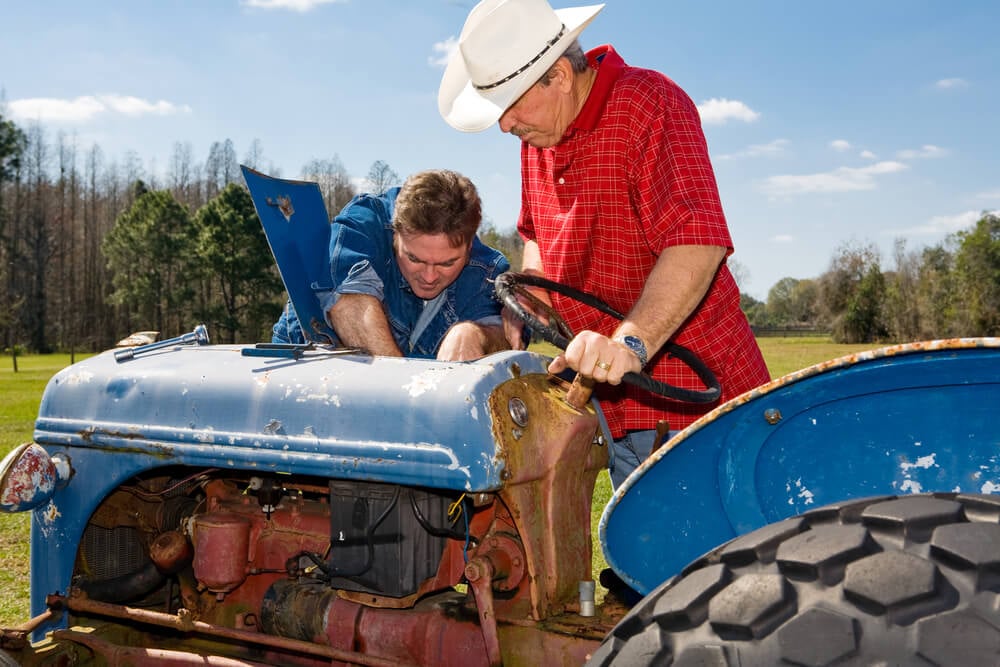 Two farmers working on a broken tractor.