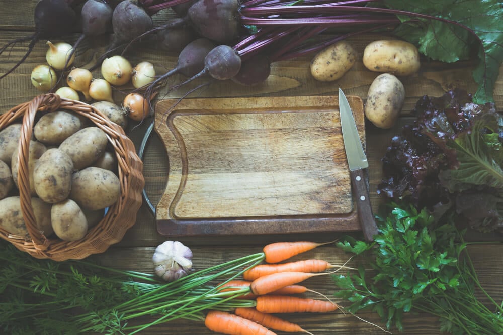 Delicious veggies like carrots and potatoes next to a cutting board.