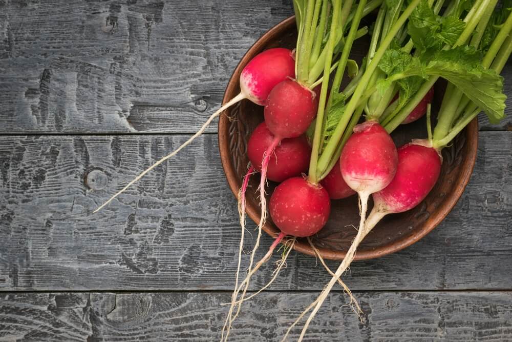 Fresh radishes in a clay bowl atop a wooden table.