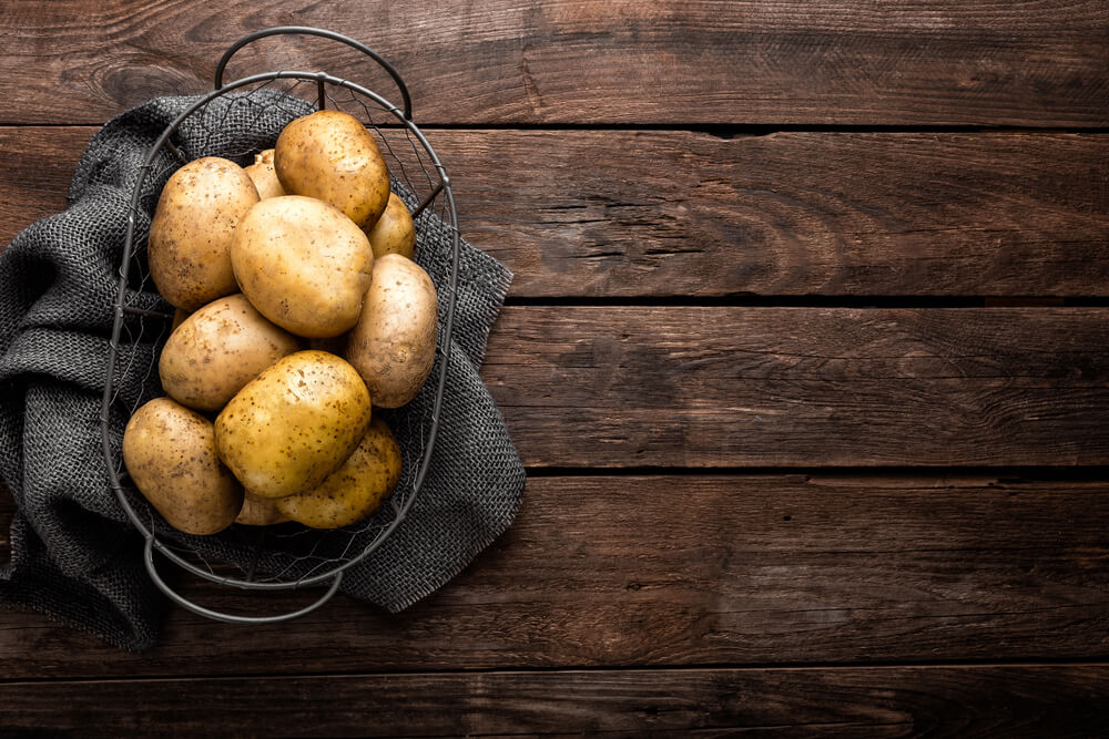 Several fresh potatoes in a basket atop a brown wooden table.