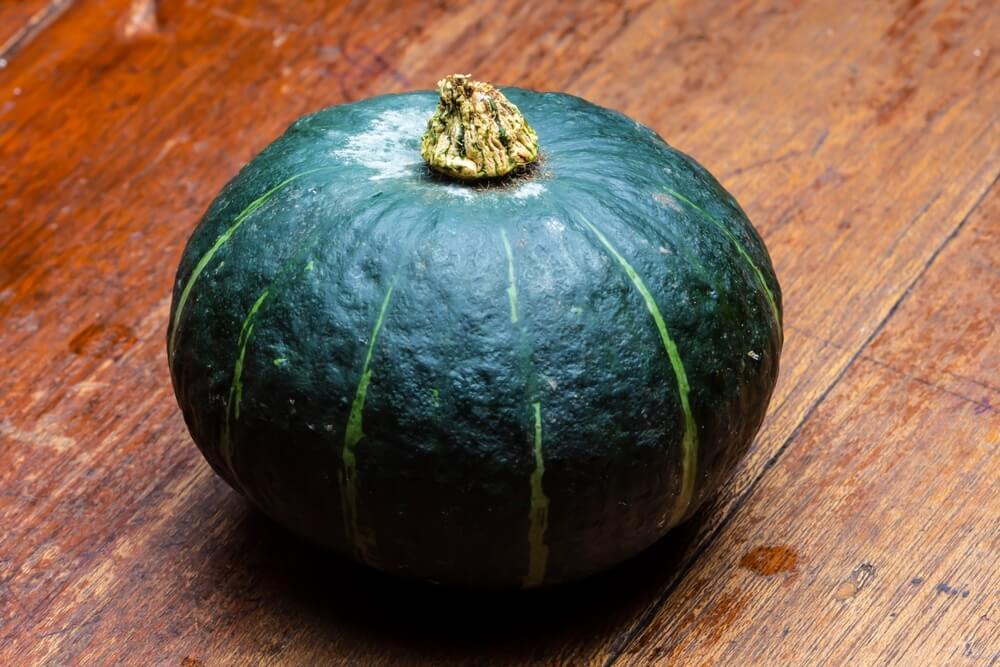 Green Kobocha winter squash pumpkin resting on a wooden table.