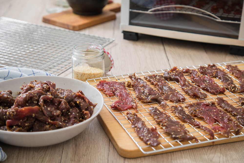 Raw marinated beef strips with sesame and chili dehydrating for delicious homemade jerky.