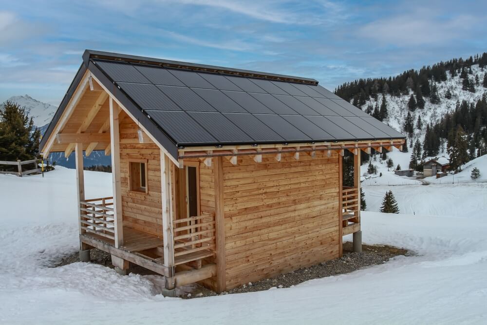 Small wooden cabin with many solar panels on the roof.