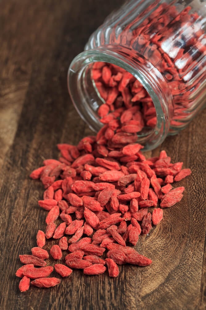 Harvested and dried goji berries in a glass bowl closeup on wooden table.