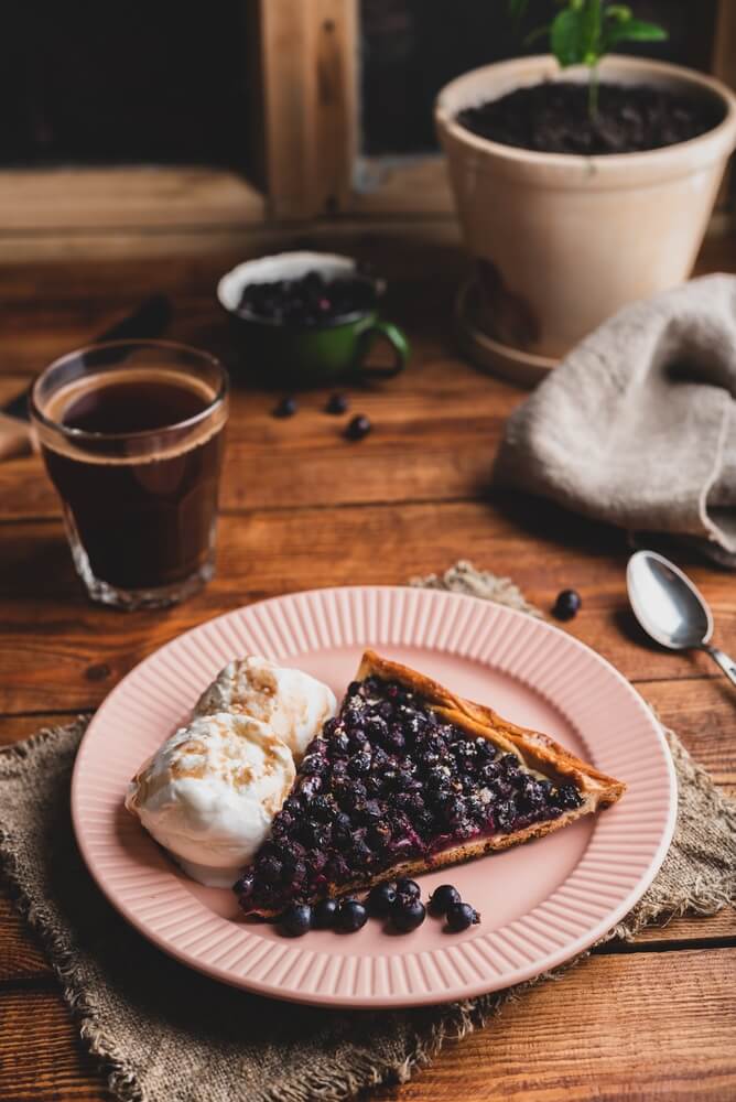 A slice of serviceberry pie with vanilla ice cream and a glass of Turkish coffee on a wooden table.