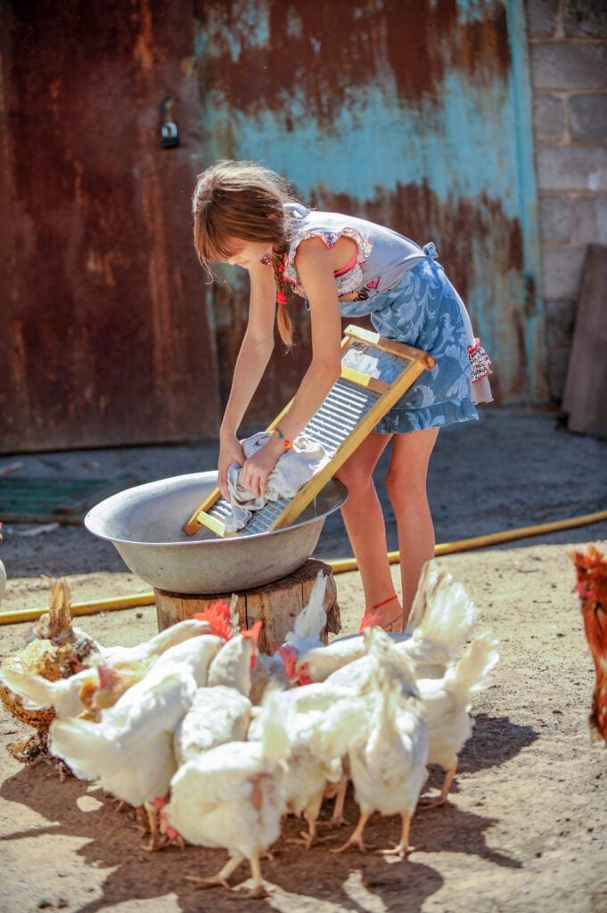 farmer's daughter is washing his father's shirt in yard. Chicken farm